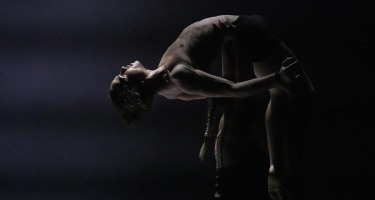 Male dancer being held up by a person in shadow. He is bent over backwards in a U shape.