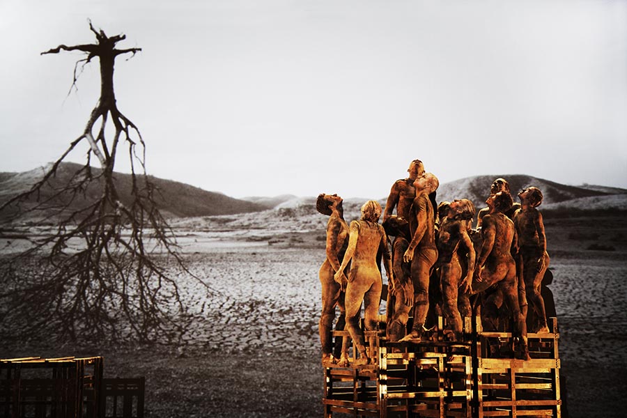 Group of dancers on ladder-like structure with projection of tree and roots in background.