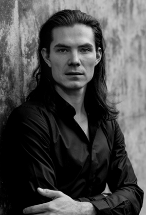 Black and white portrait of Jera Wolf, facing camera in dark button up shirt against fuzzy background.