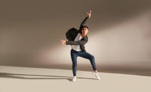 Ralph Escamillan. Man in pants, white shirt and jacket dancing with right leg slightly bent and standing on toe, left arm reaching across the front of his body, and left arm reaching up above his head.