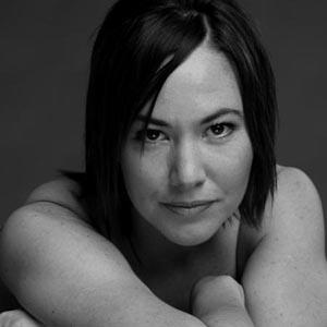 Christine Friday. A black and white headshot of a woman with straight, dark, shoulder length hair and bare shoulders facing forward, looking into the camera.