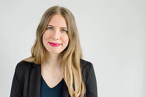 Alexandra Barker. Portrait photo of a light skinned woman with long, blonde hair and blue eyes. She is wearing a long sleeve black blazer and a necklace.