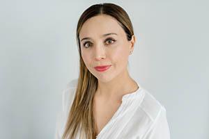 Ivy Arcos Dahm. Portrait photo of a light skinned woman with long, light brown hair and brown eyes. She is wearing a long sleeve white blouse.
