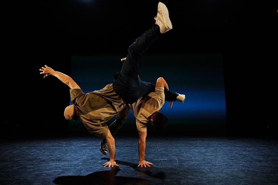 The Friday Round-Up 1 Two male dancers each balance on one hand, with their legs raised in the air. One man clasps the other's left leg with the crook of his arm.