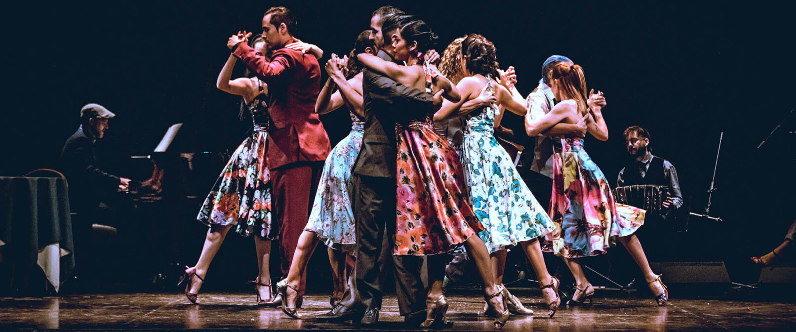 Agustina Videla. A group of mixed gender dancers in colourful dresses and suits are grouped tightly together, dancing in pairs.